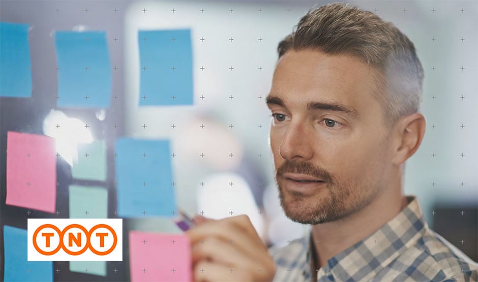Man writing on a post it note that is stuck on a window